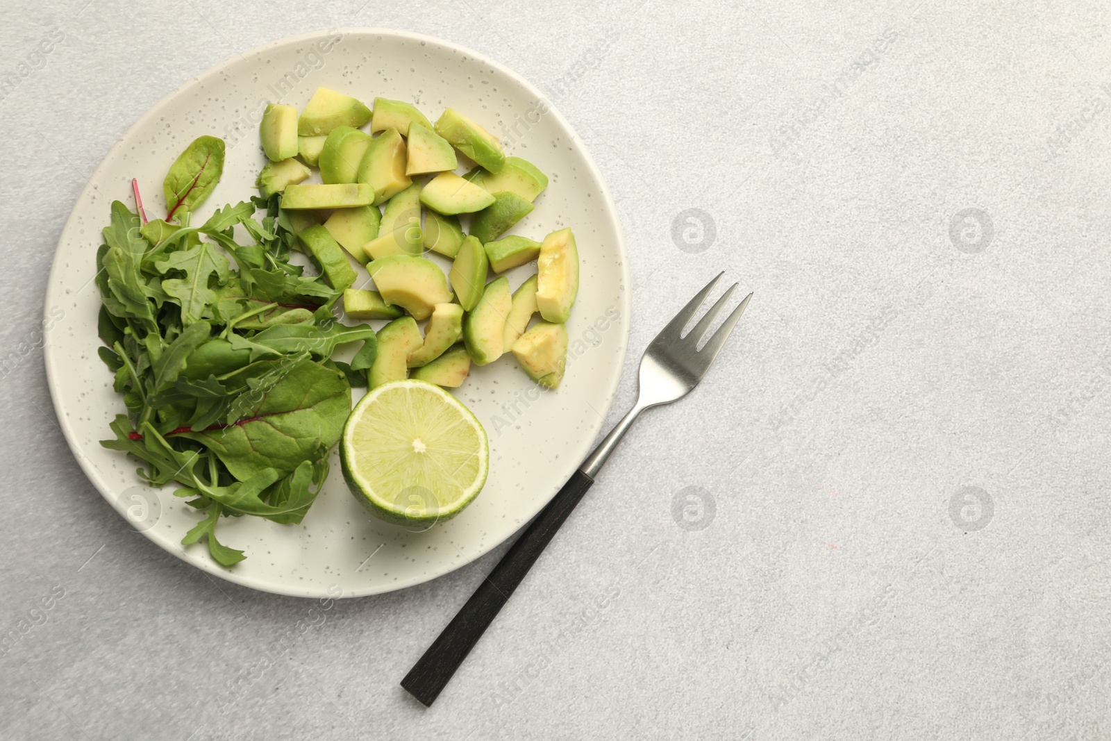 Cut ripe green avocado, greens, lime and fork on light grey table, flat lay. Space for text Photo of Cut ripe green avocado, greens, lime and fork on light grey table, flat lay. Space for text