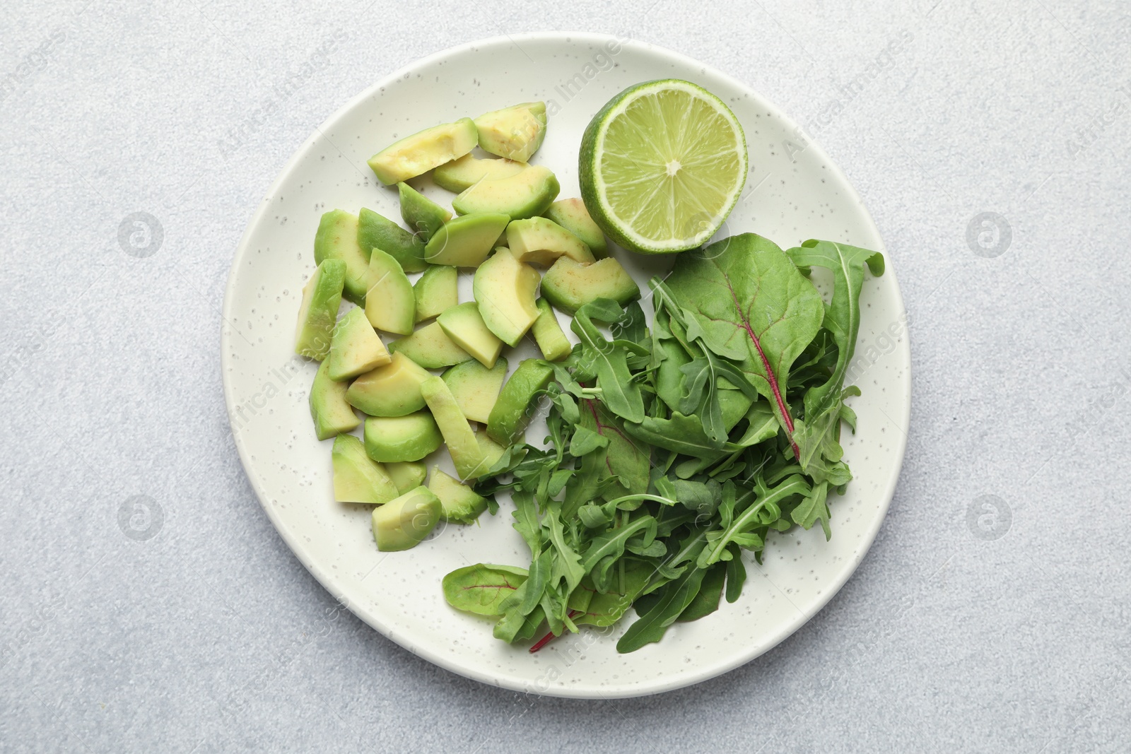 Cut ripe green avocado, greens and lime on light grey table, top view Photo of Cut ripe green avocado, greens and lime on light grey table, top view