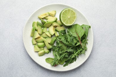 Photo of Cut ripe green avocado, greens and lime on light grey table, top view