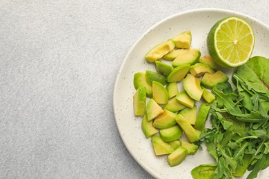 Photo of Cut ripe green avocado, greens and lime on light grey table, top view. Space for text