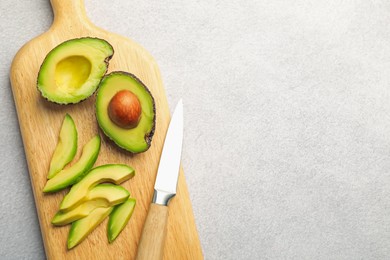 Photo of Cut ripe green avocados and knife on light grey table, top view. Space for text