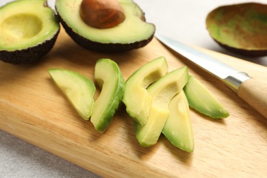 Photo of Cut ripe green avocados and knife on light grey table, closeup