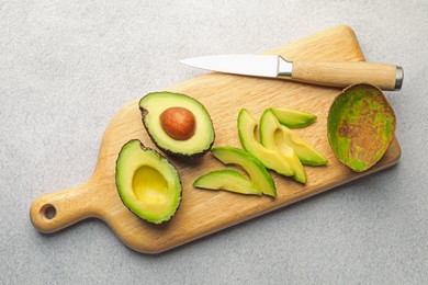 Photo of Cut ripe green avocados and knife on light grey table, top view