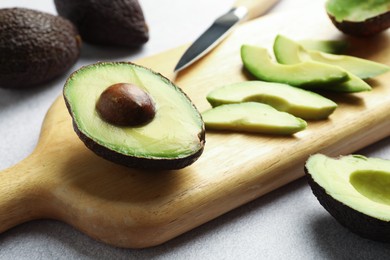 Photo of Cut ripe green avocados and knife on light grey table, closeup