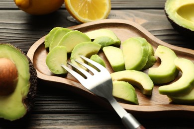 Photo of Cut ripe green avocados, lemon and fork on wooden table, closeup