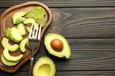 Photo of Cut ripe green avocados and fork on wooden table, flat lay. Space for text
