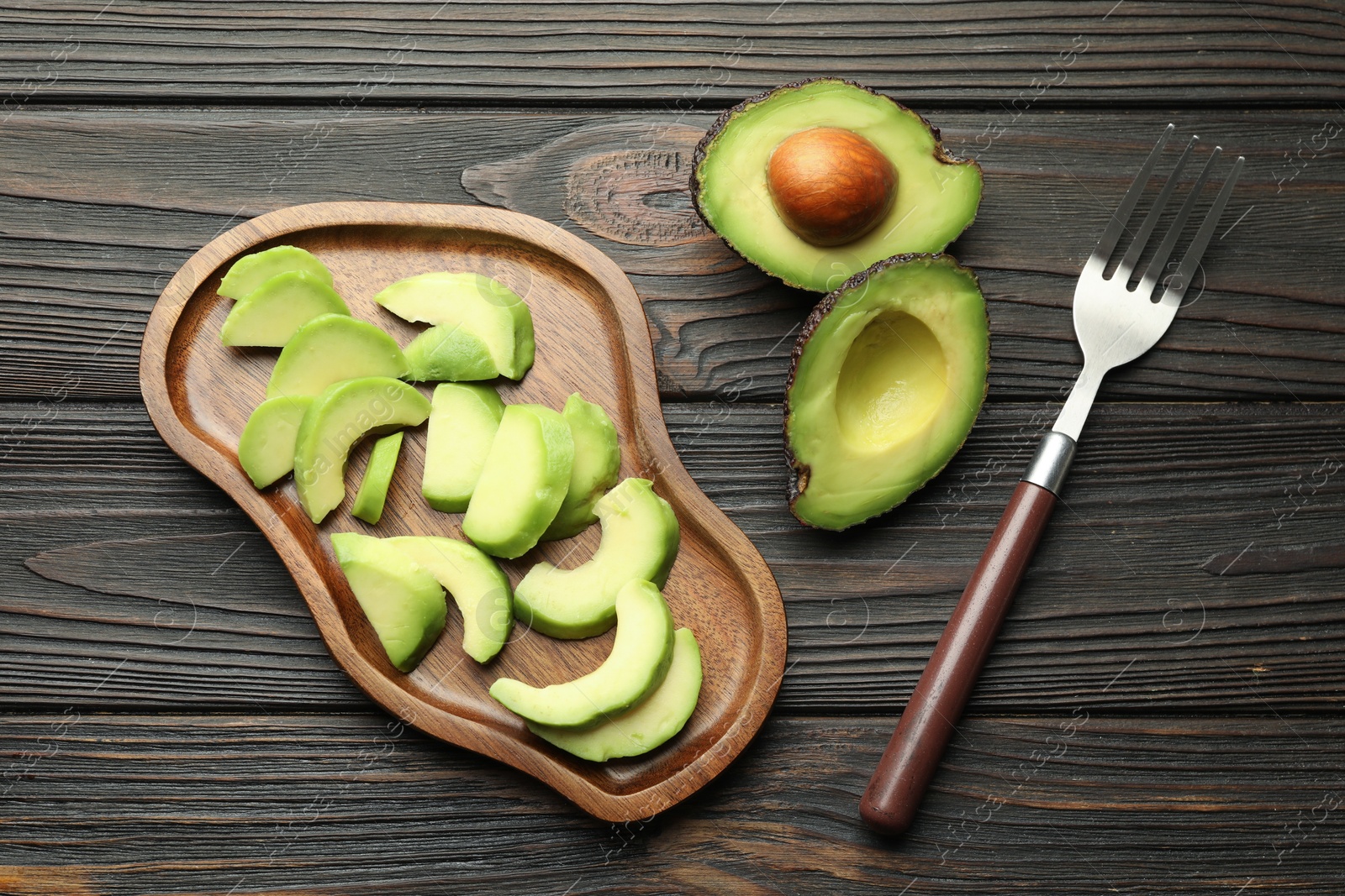 Cut ripe green avocados and fork on wooden table, flat lay Photo of Cut ripe green avocados and fork on wooden table, flat lay