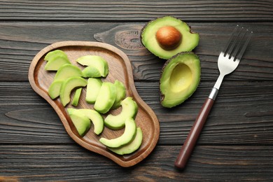 Photo of Cut ripe green avocados and fork on wooden table, flat lay