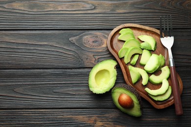 Photo of Cut ripe green avocados and fork on wooden table, flat lay. Space for text