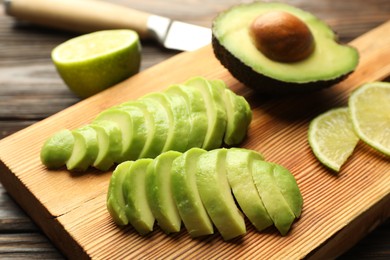 Photo of Cut ripe green avocado and lime on wooden table, closeup