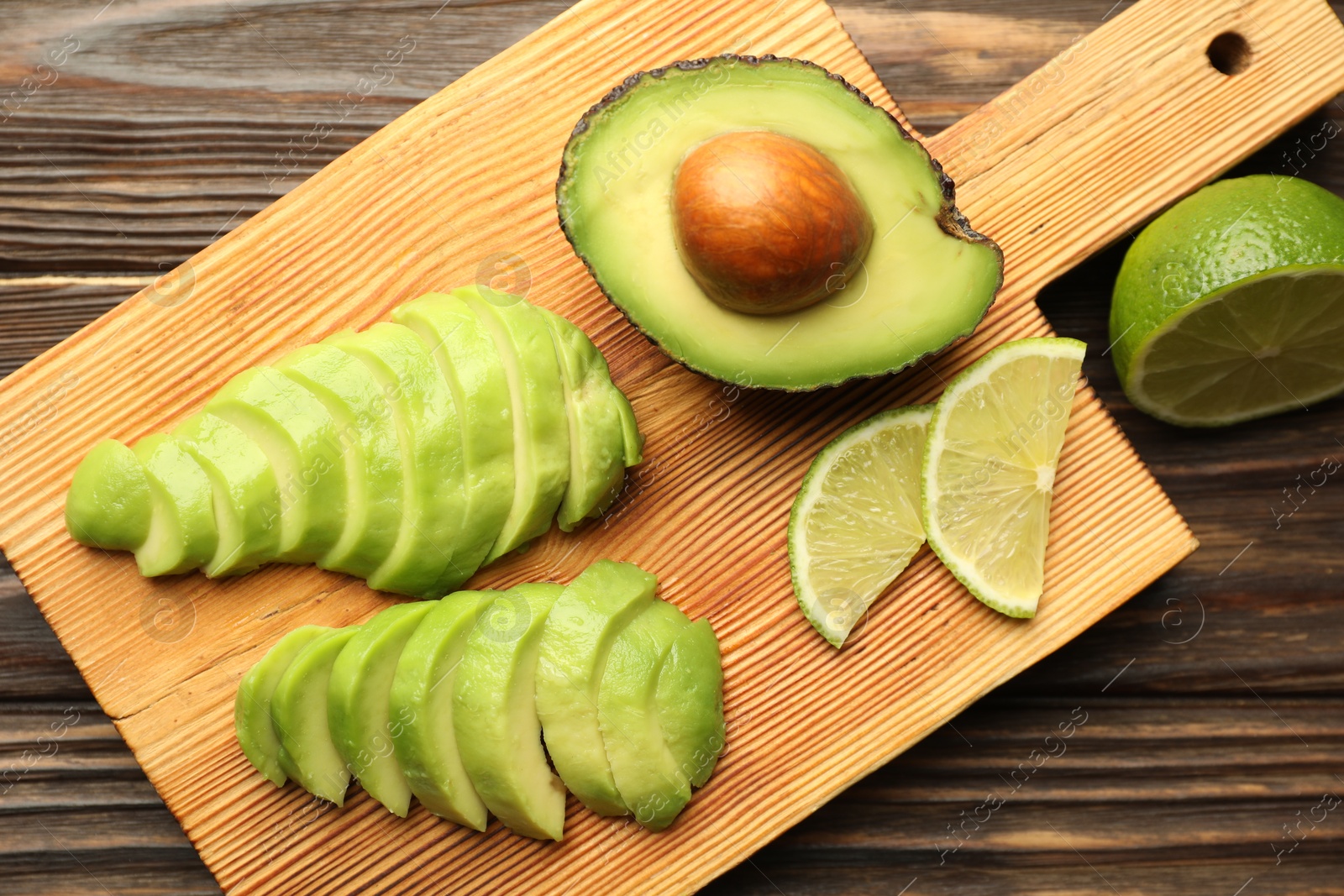 Photo of Cut ripe green avocado and lime on wooden table, flat lay