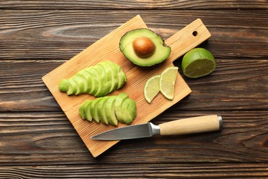 Photo of Cut ripe green avocado, lime and knife on wooden table, flat lay