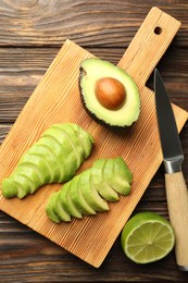 Photo of Cut ripe green avocado, lime and knife on wooden table, flat lay