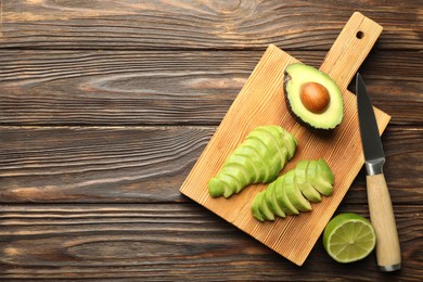 Photo of Cut ripe green avocado, lime and knife on wooden table, flat lay. Space for text