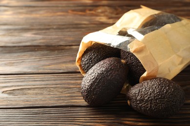 Photo of Ripe avocado fruits in paper package on wooden table, closeup. Space for text