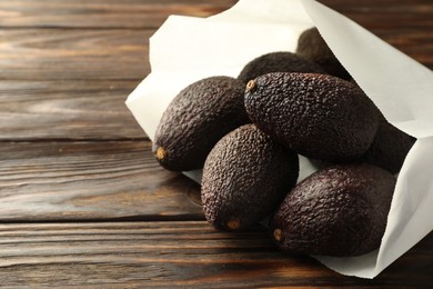 Photo of Ripe avocado fruits in paper package on wooden table, closeup. Space for text
