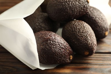 Photo of Ripe avocado fruits in paper package on wooden table, closeup