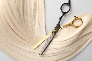 Photo of Blonde hair lock and scissors on light grey background, top view