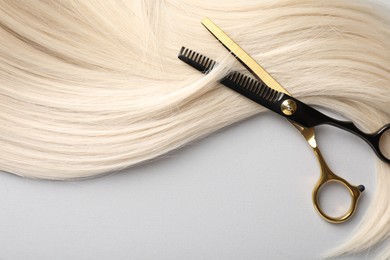Photo of Blonde hair lock and scissors on light grey background, top view