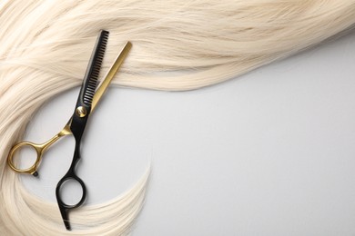 Photo of Blonde hair lock and scissors on light grey background, top view. Space for text