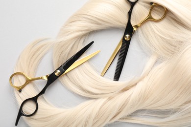 Photo of Blonde hair locks and scissors on light grey background, flat lay