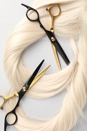 Photo of Blonde hair locks and scissors on light grey background, flat lay