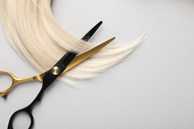 Photo of Blonde hair lock and scissors on light grey background, top view. Space for text