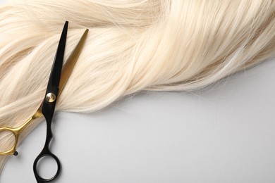 Photo of Blonde hair lock and scissors on light grey background, top view
