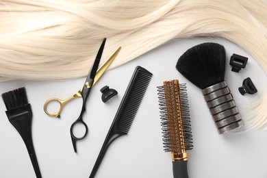 Photo of Different hairdresser's tools and blonde hair lock on light grey background, flat lay