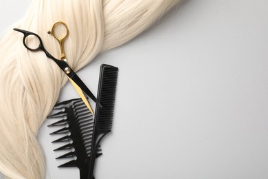 Photo of Different hairdresser's tools and blonde hair lock on light grey background, flat lay. Space for text