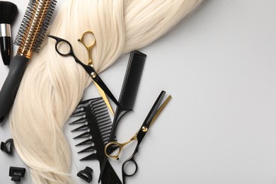 Photo of Different hairdresser's tools and blonde hair lock on light grey background, flat lay. Space for text