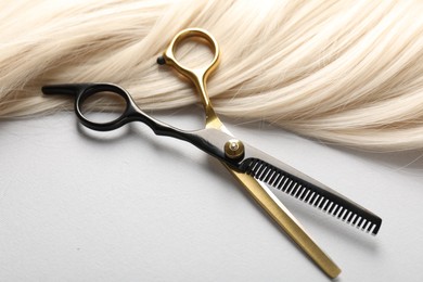 Photo of Blonde hair lock and scissors on light grey background, closeup