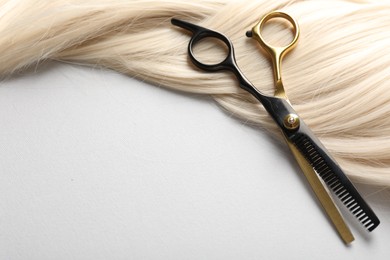 Photo of Blonde hair lock and scissors on light grey background, closeup