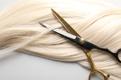 Photo of Blonde hair lock and scissors on light grey background, above view