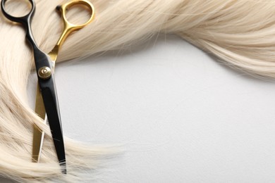 Photo of Blonde hair lock and scissors on light grey background, closeup