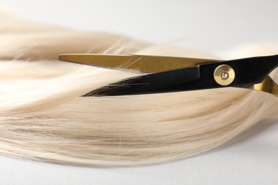Photo of Cutting blonde hair lock with scissors on light grey background, closeup