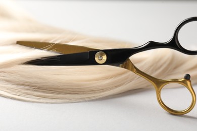 Photo of Cutting blonde hair lock with scissors on light grey background, closeup
