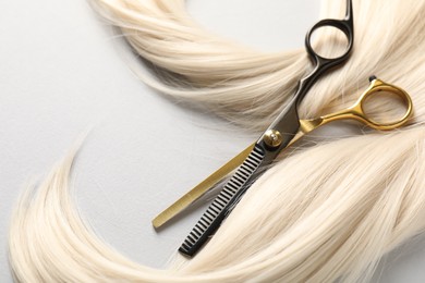 Photo of Blonde hair lock and scissors on light grey background, closeup