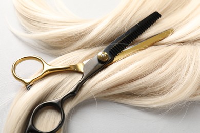 Photo of Blonde hair lock and scissors on light grey background, closeup