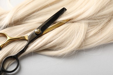 Photo of Blonde hair lock and scissors on light grey background, closeup