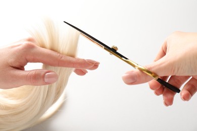 Photo of Hairdresser cutting blonde hair lock with scissors on light grey background, closeup
