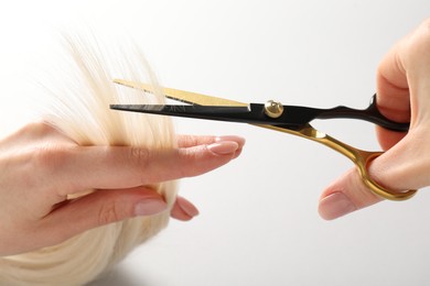 Photo of Hairdresser cutting blonde hair lock with scissors on light grey background, closeup