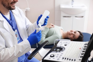 Photo of Sonographer applying gel on ultrasound transducer and woman waiting for examination in clinic, selective focus
