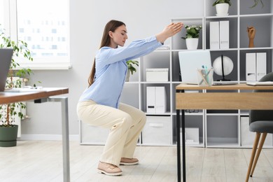Photo of Beautiful woman doing exercise near desk in office