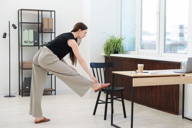 Photo of Beautiful woman exercising with chair in office