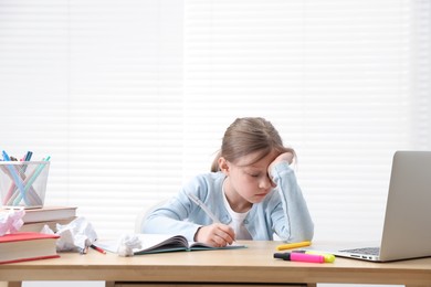 Photo of Tired little girl doing homework at table indoors