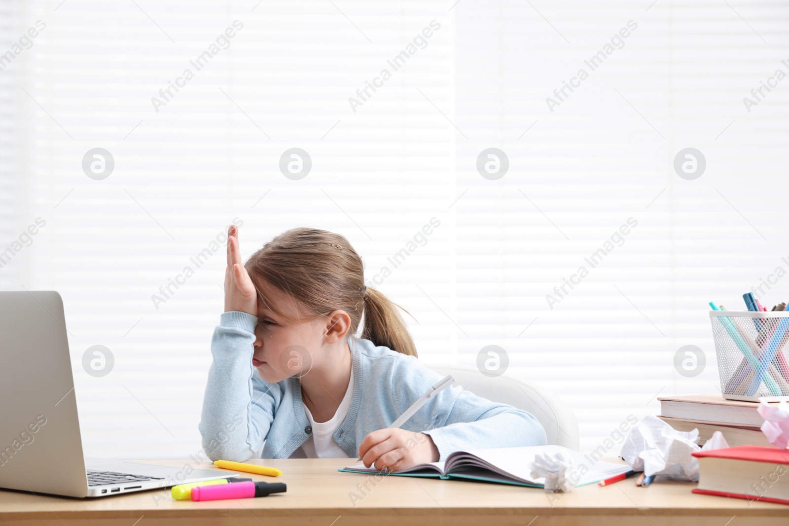 Tired little girl doing homework at table indoors Photo of Tired little girl doing homework at table indoors