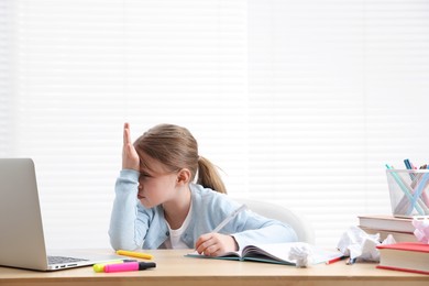 Photo of Tired little girl doing homework at table indoors
