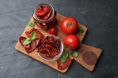 Photo of Tasty sun dried tomatoes and fresh vegetables on black table, top view