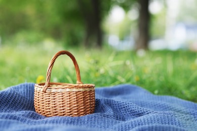 Photo of Wicker basket and blanket on green grass outdoors. Space for text